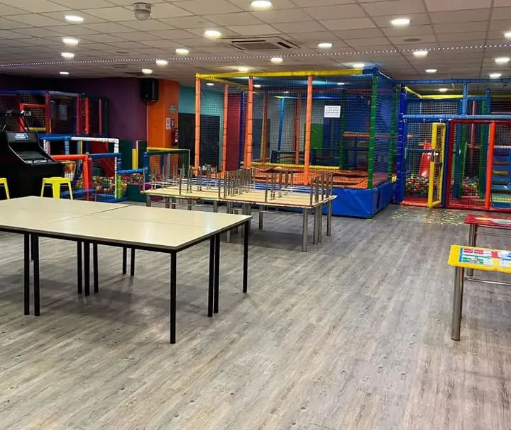 Sala amplia con mesas, máquina recreativa y estructuras de juego al fondo