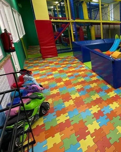 Zona de juego con suelo de puzle, estructura roja y correpasillos